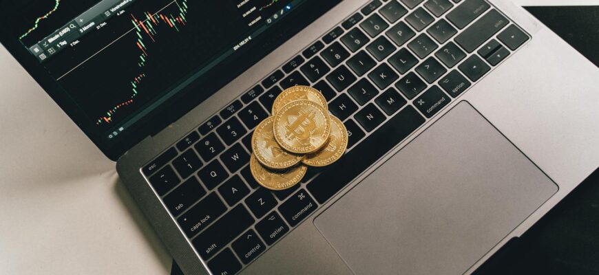 Bitcoin coins placed on a laptop keyboard while a trading chart displays on the screen, showcasing digital finance.