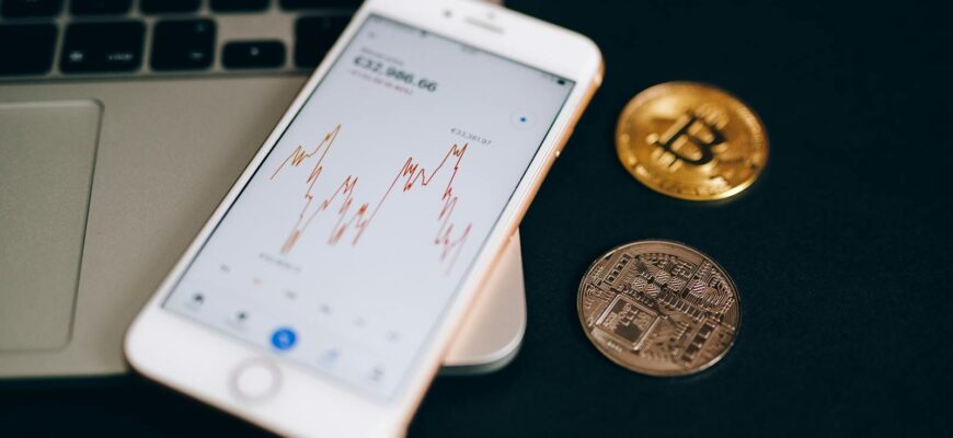 Close-up view of cryptocurrency coins and stock market graph on a smartphone screen.