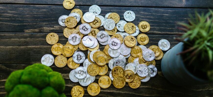 Gold and silver bitcoin coins mixed on a wooden surface with potted plants.